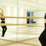 Femeie exersand la o sedinta specifică de Barre, privindu-se in oglinda