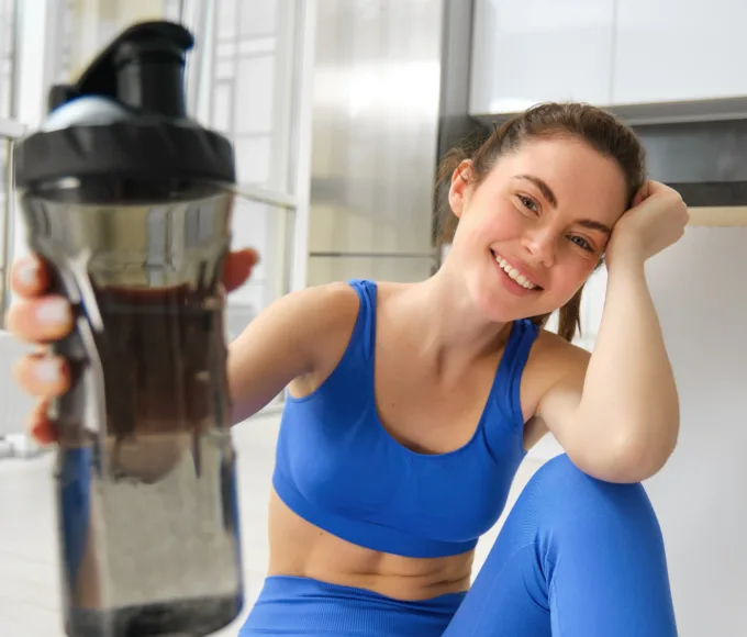 femeie la sala de fitness consumand cafea