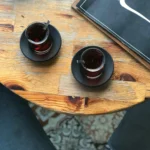 doua cani de ceai, negru si verde, pe o masa a unei terase, afara